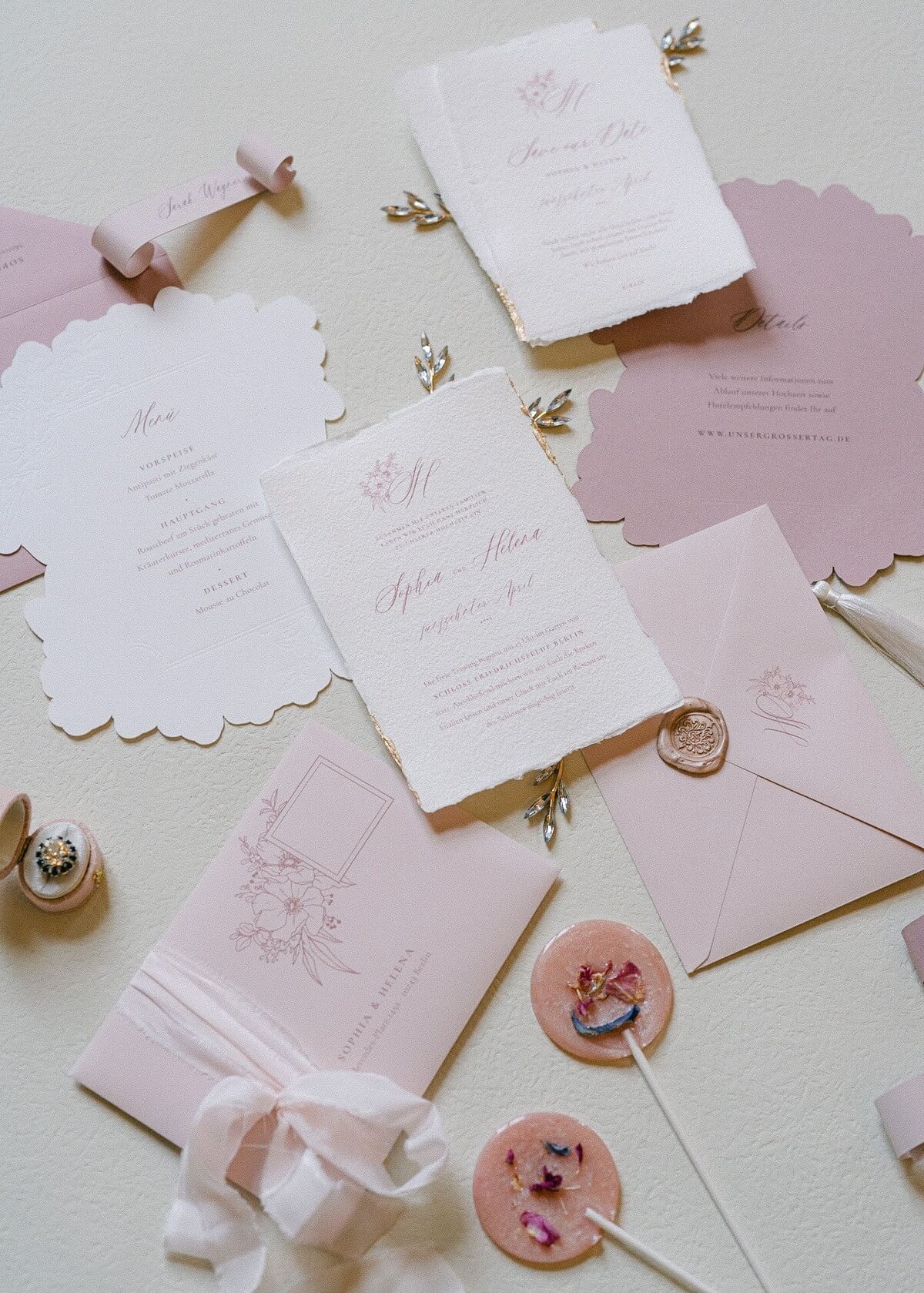 Finely designed flatlay of wedding invitations and menu cards in pastel shades with golden sealing wax sealing and floral accents on a light background for a wedding at Schloss Friedrichsfelde Berlin.