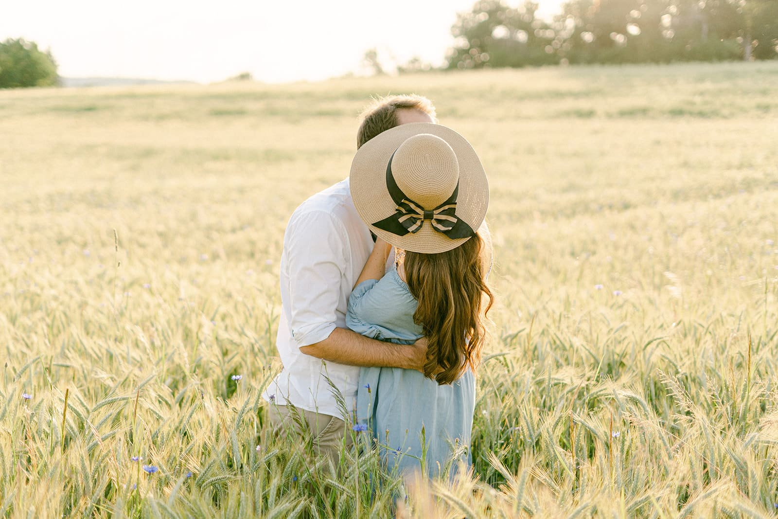 Couple at engagement session photo embrace and hold hat in front of their faces