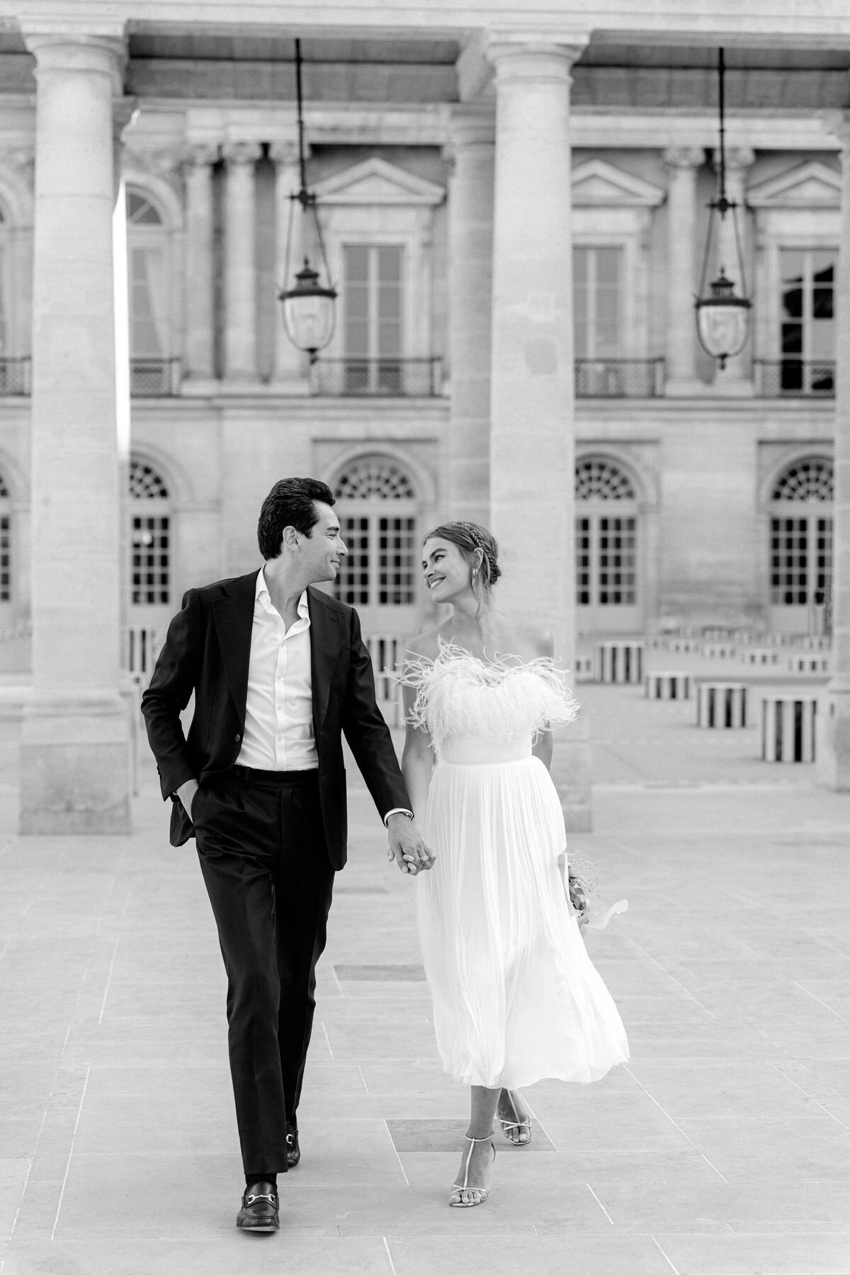 Hochzeitsfoto Brautpaar läuft lachend auf Kamera zu in den Colonnes de Buren in Paris