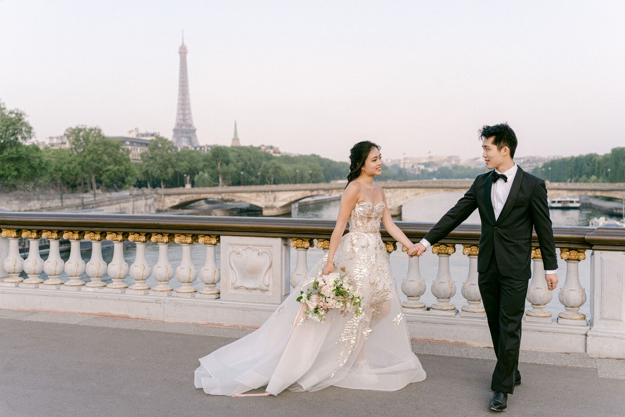 Bride and groom walking holding hands on Pont Alexandre Paris