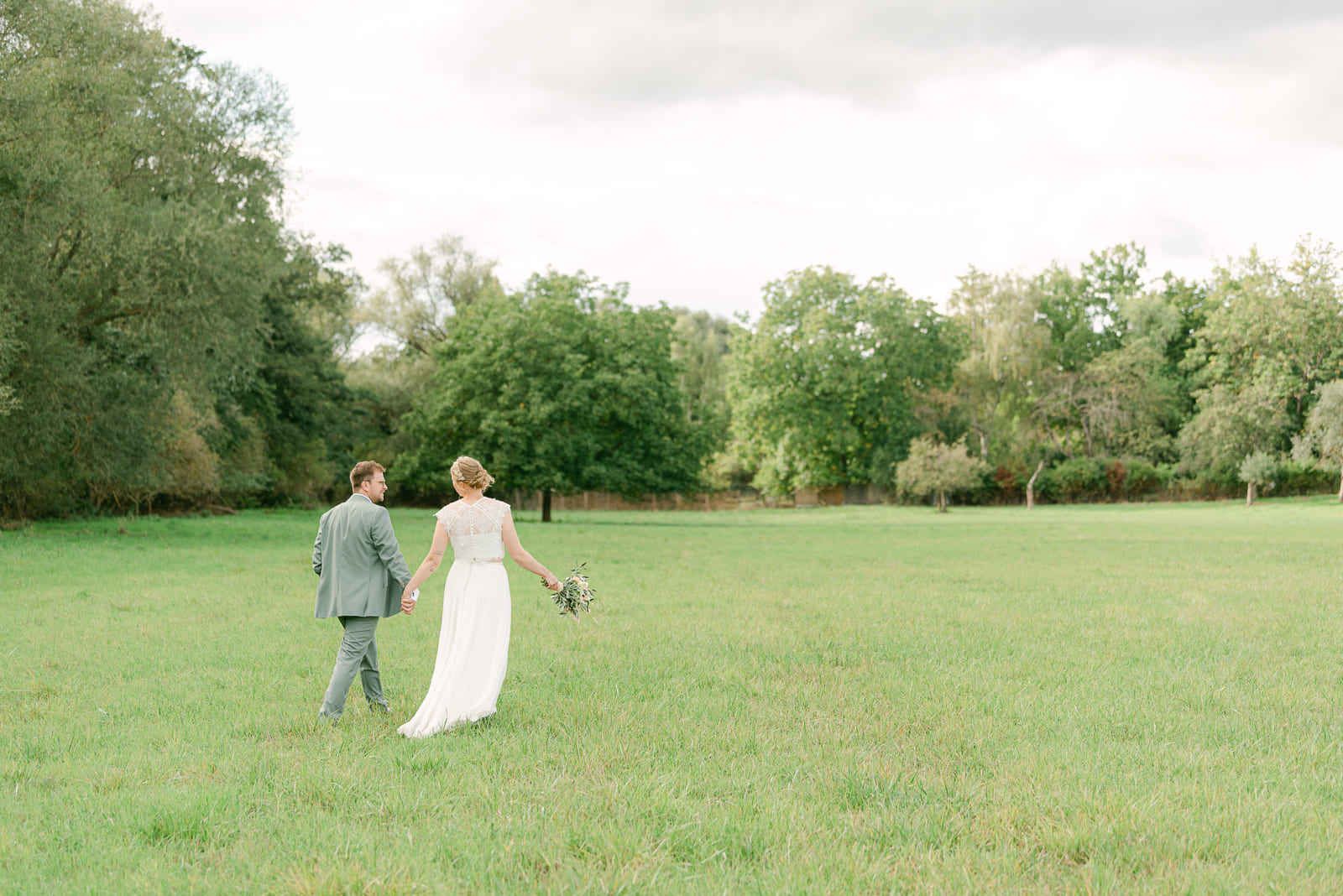 Wedding couple on meadow walking away from camera holding hands