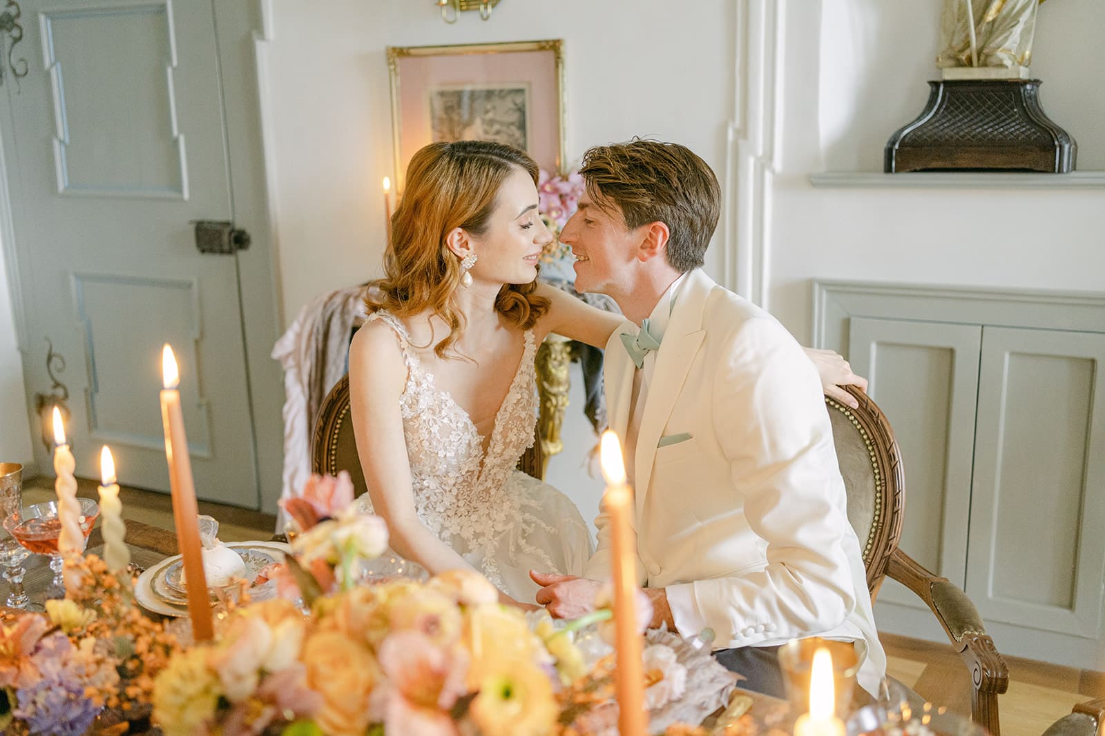 Brautpaar sitzt lächelnd an Tisch mit Hochzeitsdekoration mit farbenfrohen Blumen und Kerzen