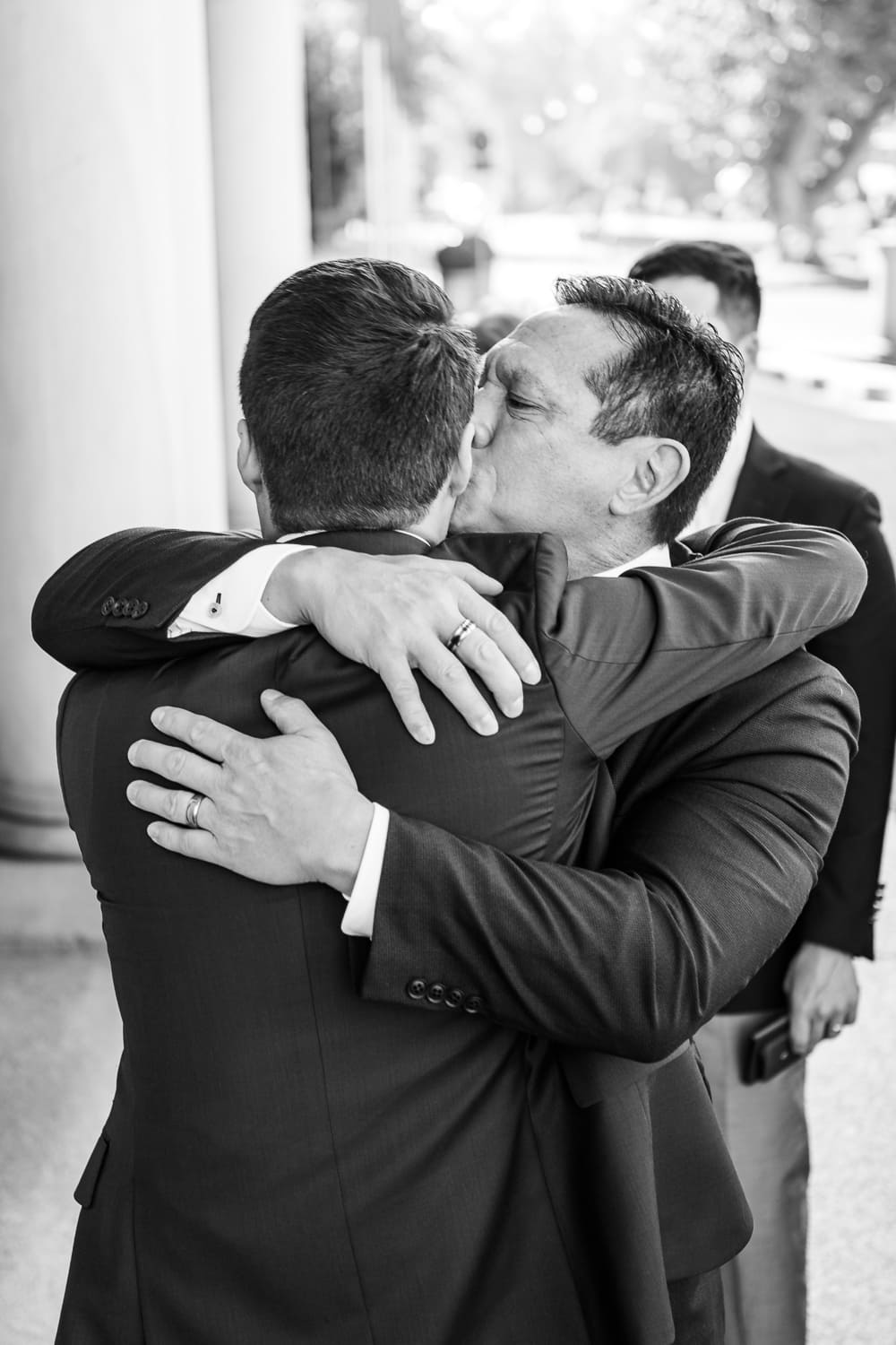 Vater des Bräutigams gibt Bräutigam Kuss auf die Wange nach emotionaler Trauung